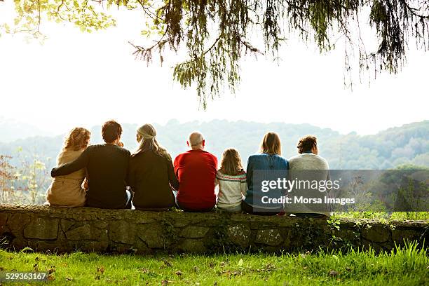 multi-generation family relaxing on retaining wall - familia de dos generaciones fotografías e imágenes de stock