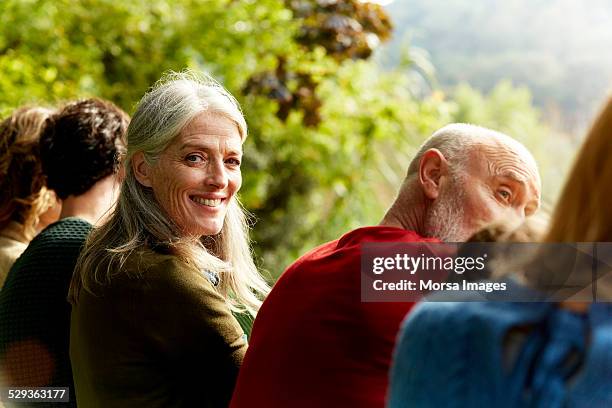 senior woman sitting with family at park - mirar por encima del hombro mujer fotografías e imágenes de stock