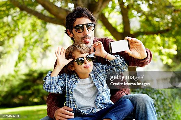 playful father and son taking selfie in park - father son going out stock pictures, royalty-free photos & images