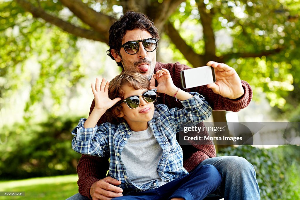 Playful father and son taking selfie in park