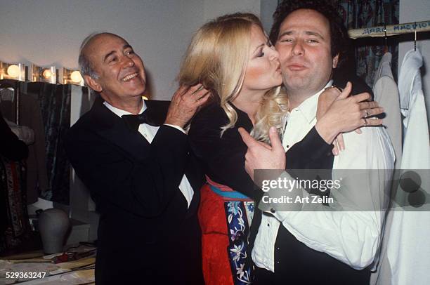 Rob Reiner being kissed on the cheek by Sally Struthers in their dressing room with Carl Reiner holding her hair back.; circa 1970; New York.