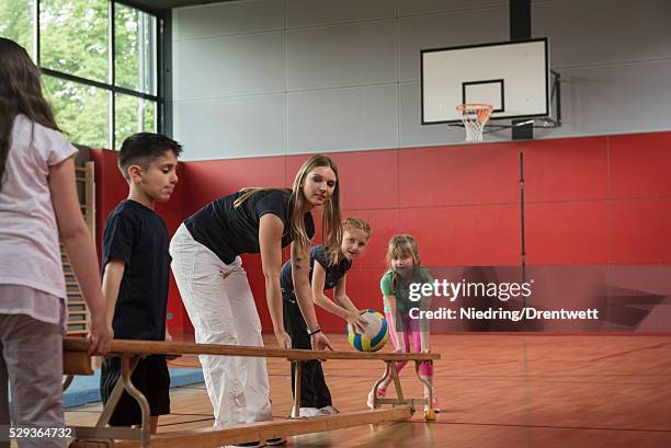 teacher and students carrying bench in sports hall, munich, bavaria, germany - school gymnastics stock-fotos und bilder