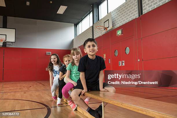 children resting on bench before exercises in large gym of school, bavaria, munich, germany - kurdish girl stock pictures, royalty-free photos & images