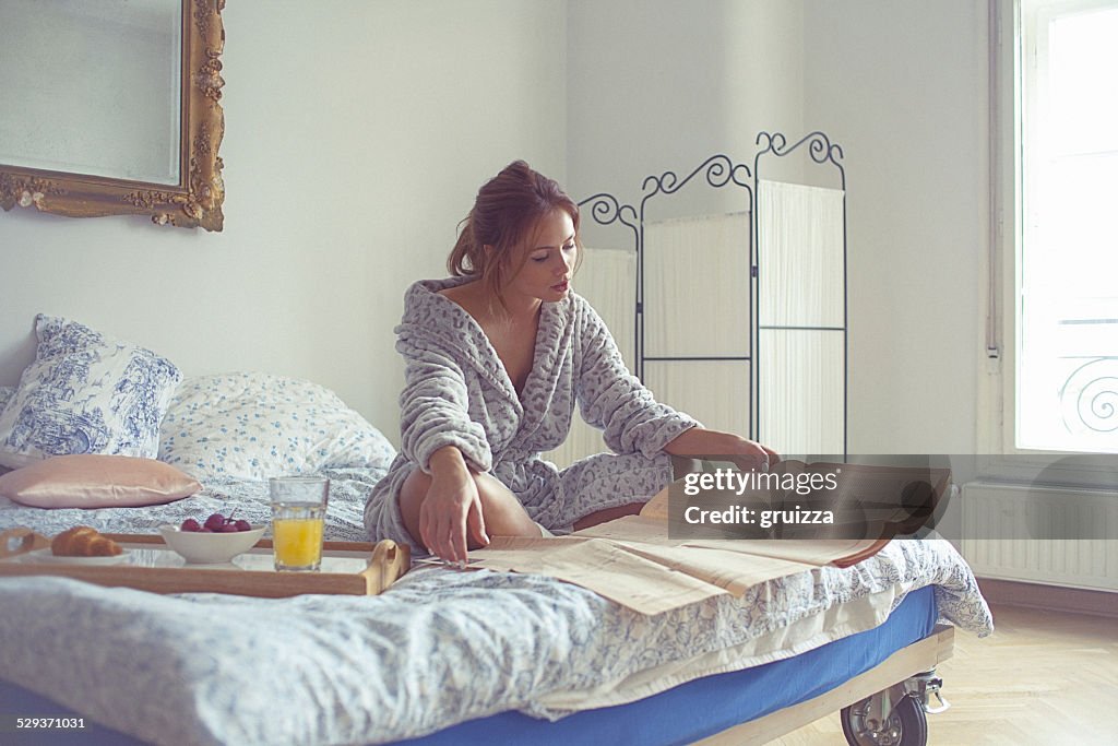 Beautiful young woman having breakfast and reads newspaper on be
