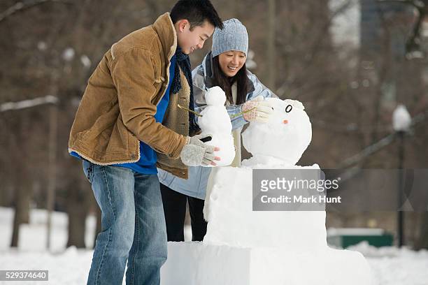 couple making a snowman in a public park - boston winter stock pictures, royalty-free photos & images