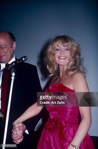 Goldie Hawn holding hands with Mayor Ed Kock behind a microphone; circa 1980; New York.