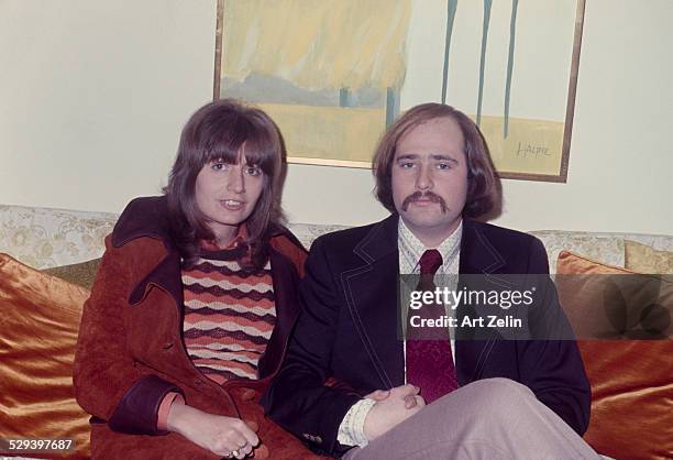 Rob Reiner with his wife Penny Marshall sitting on a sofa. She is wearing a rust suede coat; circa 1970; New York.