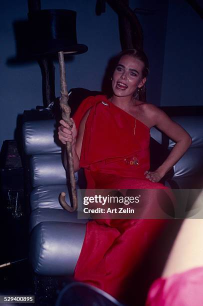 Margaux Hemingway wearing a red dress holding a cane and top hat; circa 1970; New York.