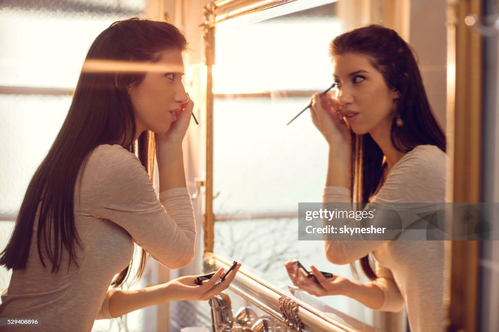 Young woman applying make-up in bathroom.