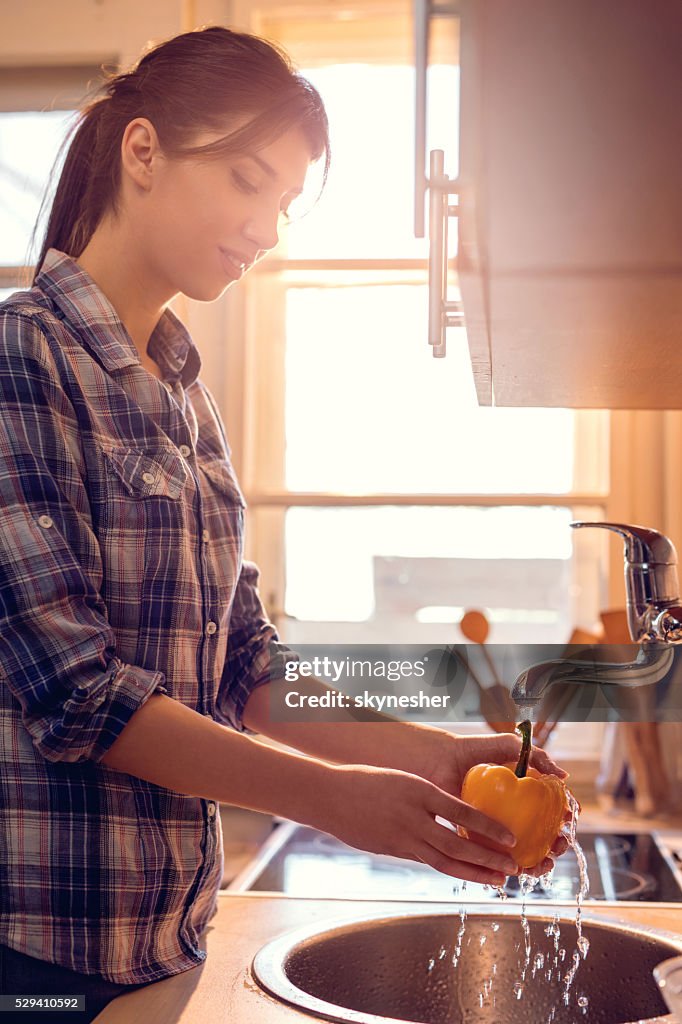 Smiling woman washing pepper in the kitchen.