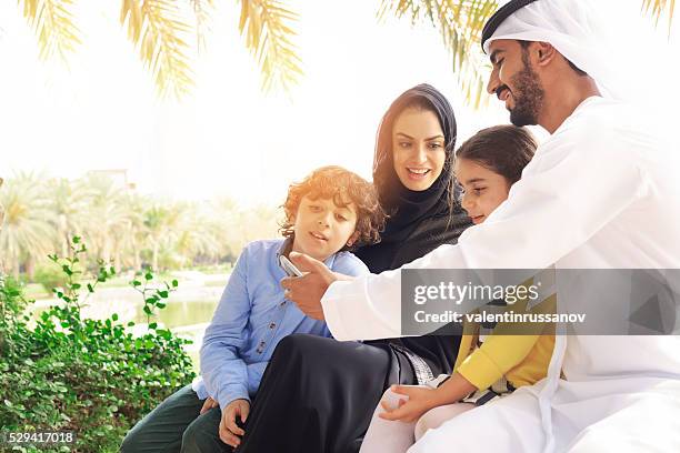 arab family looking pictures on phone in the park - happy arab family on travel stock pictures, royalty-free photos & images