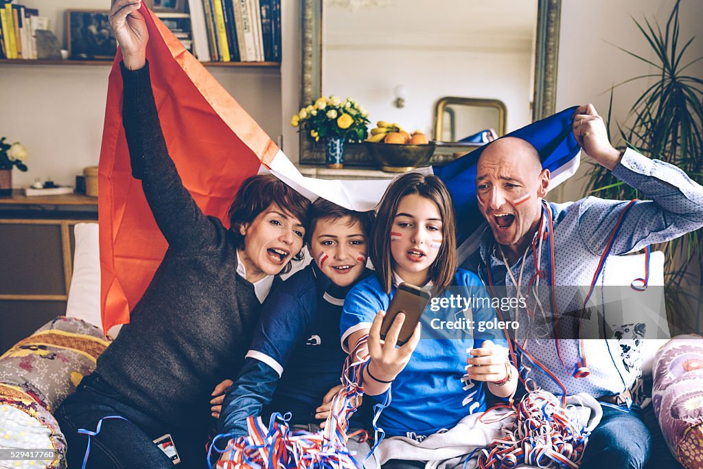 French family with flag watching soccer game on smartphone