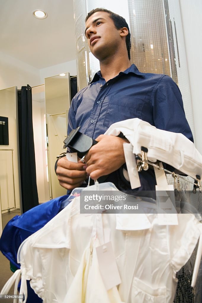 Teen boy holding clothing on hangers in store