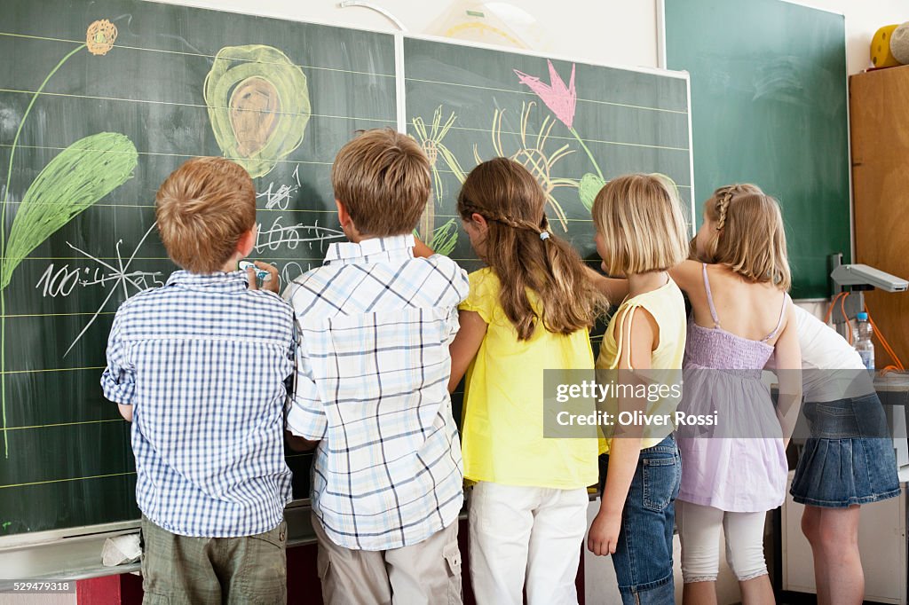 Children writing and drawing on blackboard