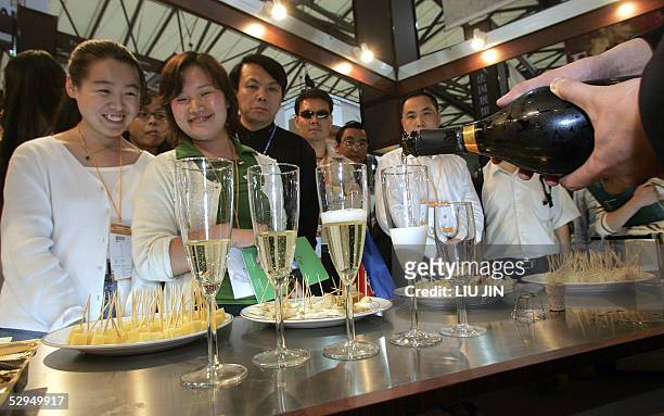 Visitors watch a service man pouring the cups of champagne at an international food exhibition in Shanghai, 19 May 2005. AFP PHOTO/LIU Jin