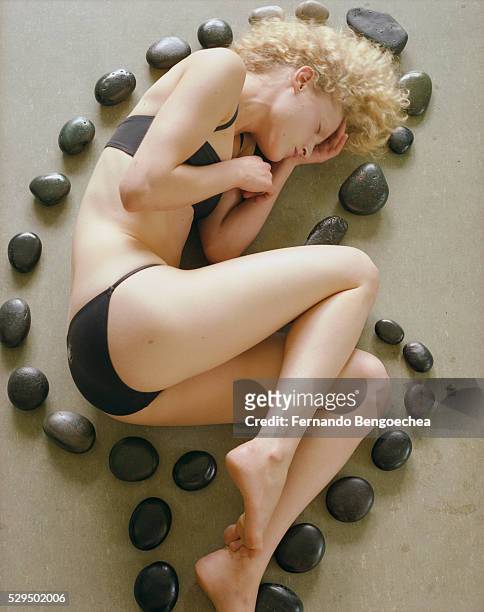 woman lying on floor surrounded by hot stone massage equipment - circondare foto e immagini stock
