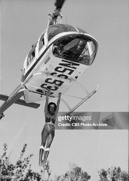 An unidentified stuntwoman, dressed as Wonder Woman, hangs from the landing struts of an airborne helicopter in an outtake from an episode from the...