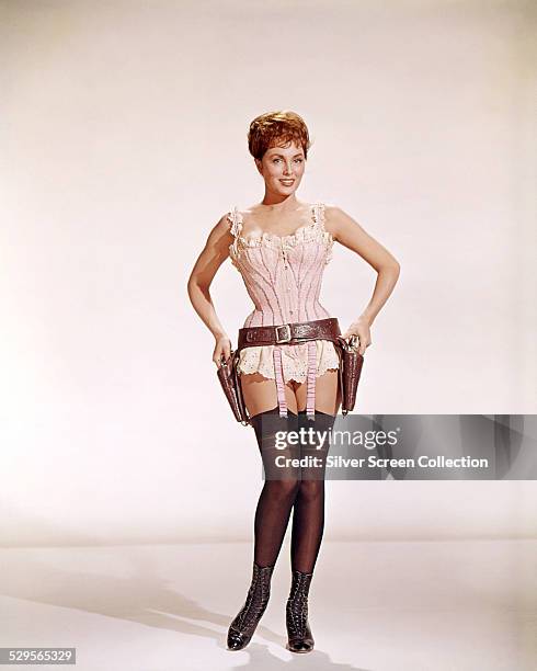 American actress Charlene Holt wearing stockings, a corset and a gun belt in a promotional portrait for 'El Dorado', directed by Howard Hawks, 1966.