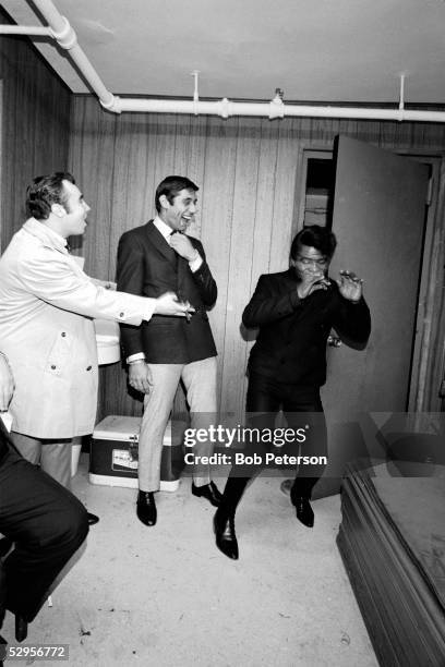 American professional football player Joe Namath laughs as rhythm and blues, soul, and funk musician James Brown demonstrates dance moves, 1966.