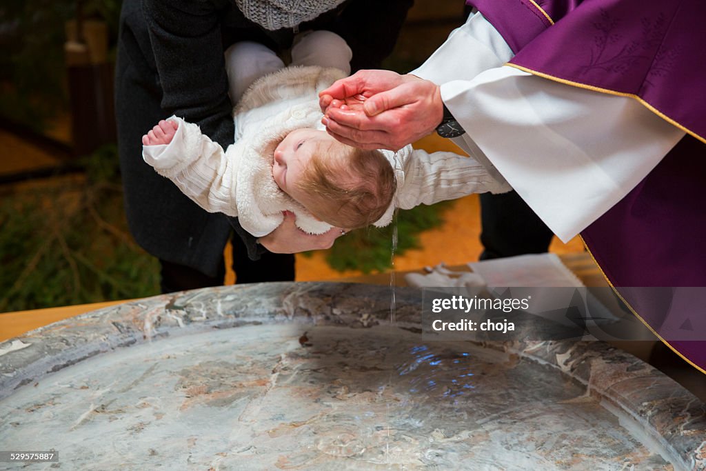 Priest is baptizing little baby girl in a church