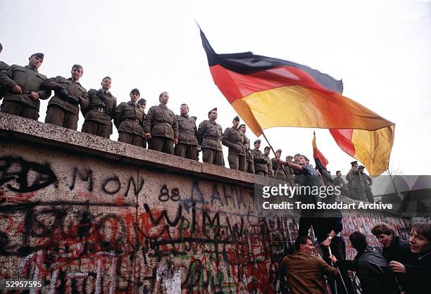 East German border guards try to prevent a crowd climbing onto the Berlin Wall on the morning that the first section was pulled down. This is a...