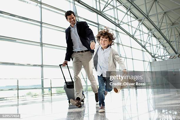 father and son (5-6) running across airport lobby - airport stockfoto's en -beelden