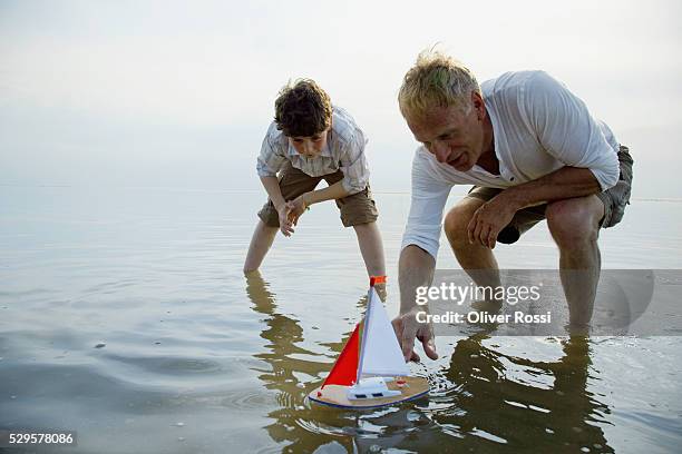 grandfather and grandson playing with a model sailboat - toy boat stock pictures, royalty-free photos & images