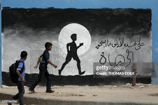 Two Palestinian schoolboys walk past a graffiti painted on a wall of the United Nations school of Beit Hanun, in the northern Gaza Strip, on May 9,...