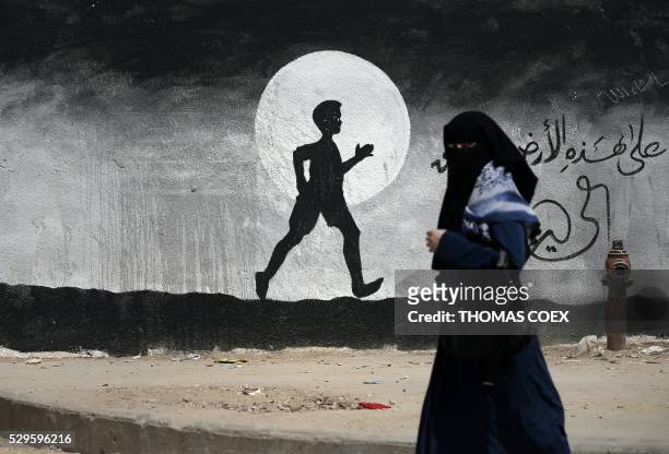Palestinian woman walks past a graffiti painted on a wall of the United Nations school of Beit Hanun, in the northern Gaza Strip, on May 9, 2016.