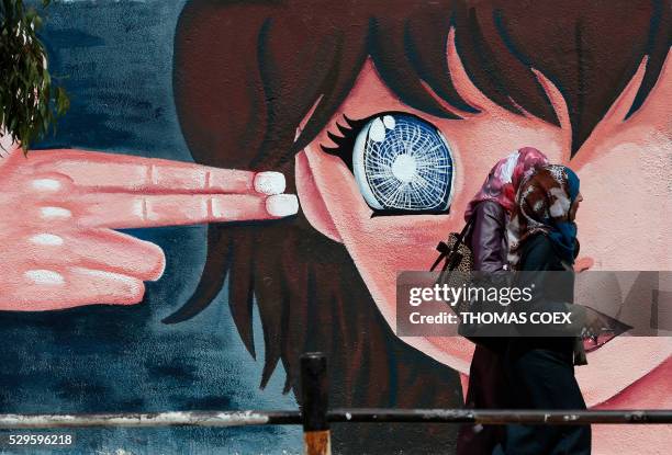 Two Palestinian women walk past a graffiti painted on a wall of the United Nations school of Beit Hanun, in the northern Gaza Strip, on May 9, 2016.