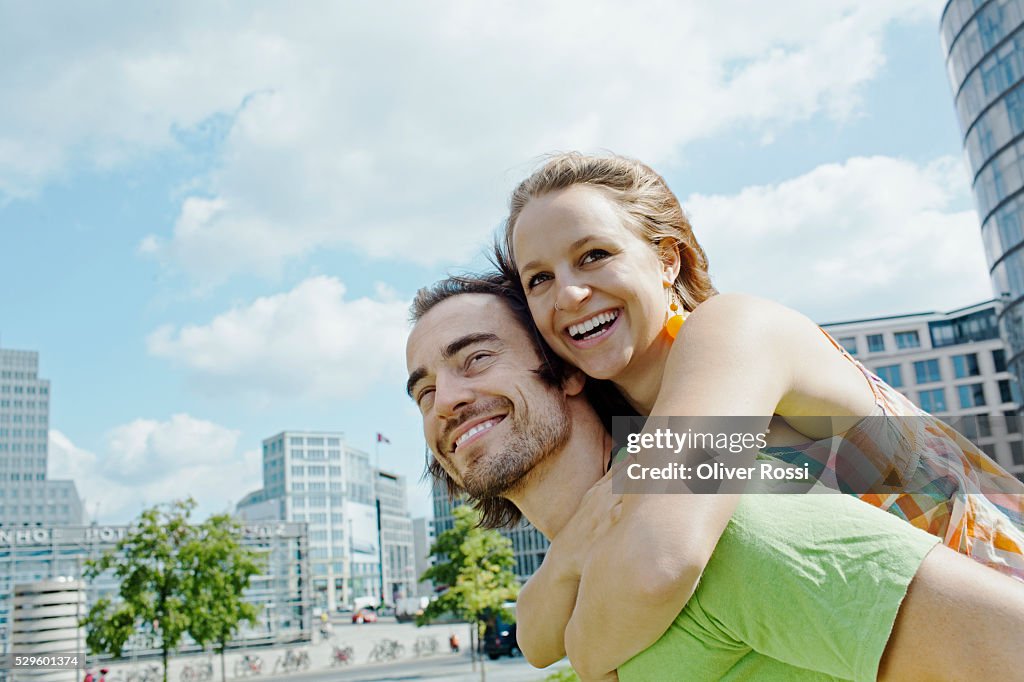 Young man giving piggy back ride to woman in city