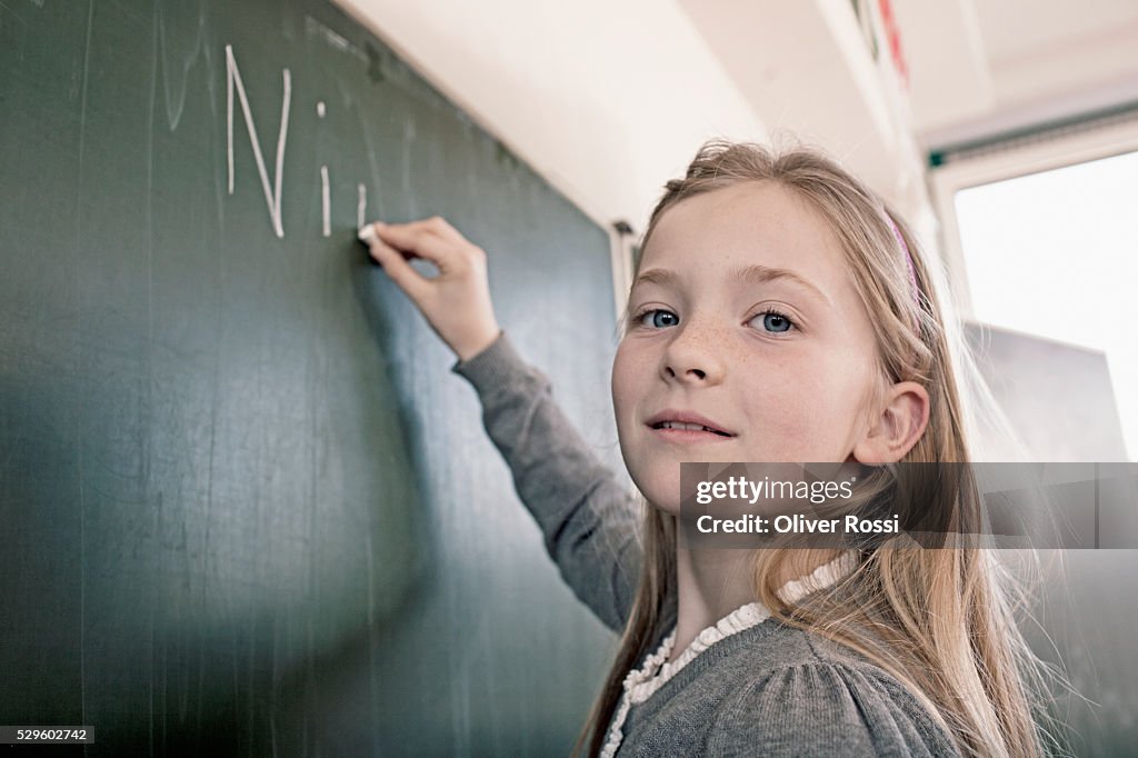 Happy young schoolgirl (8-9) writing on blackboard