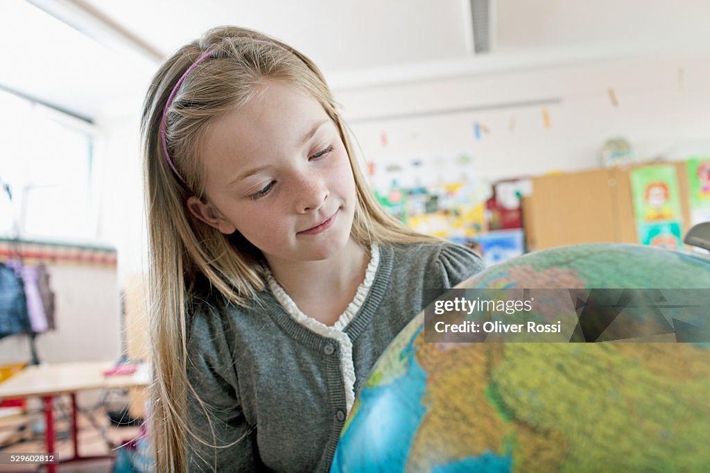 Happy young schoolgirl (8-9) looking at globe