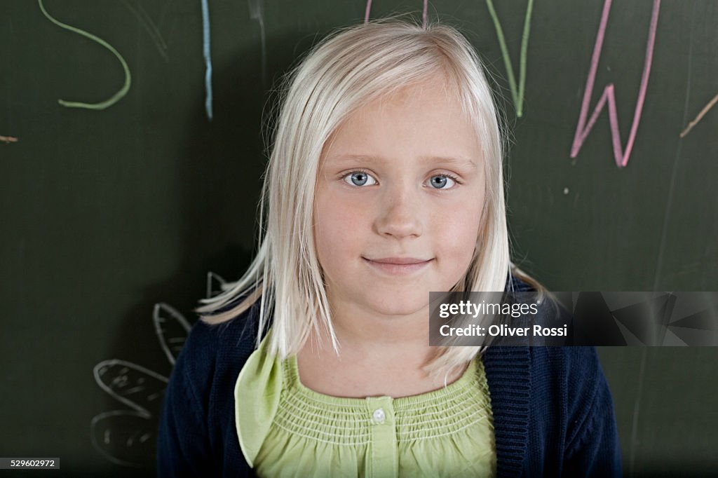 Happy young schoolgirl (8-9) posing against blackboard