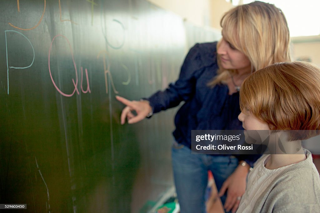 Female teacher and young school boy (6-7) standing by blackboard