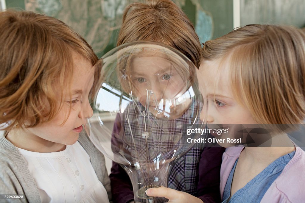 Two girls (6-7) and boy (8-9) looking at large light bulb