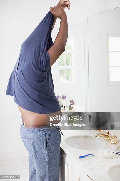 man taking off shirt in bathroom - spogliarsi foto e immagini stock
