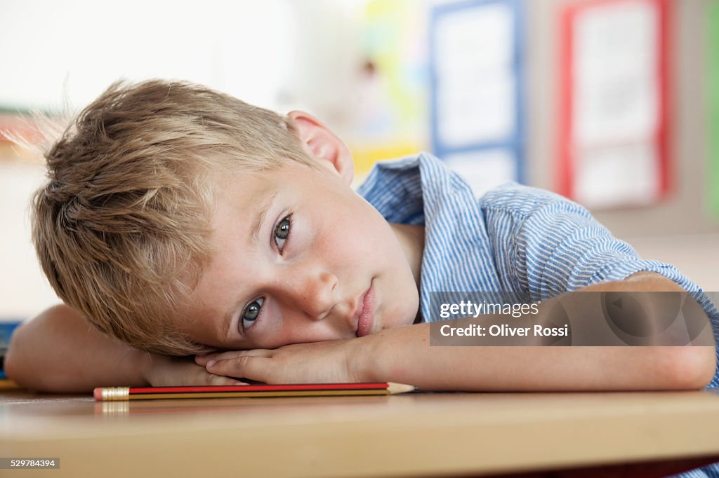 Boy resting on desk in classroom