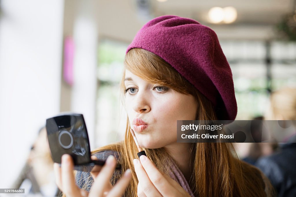 Young woman applying makeup in cafe