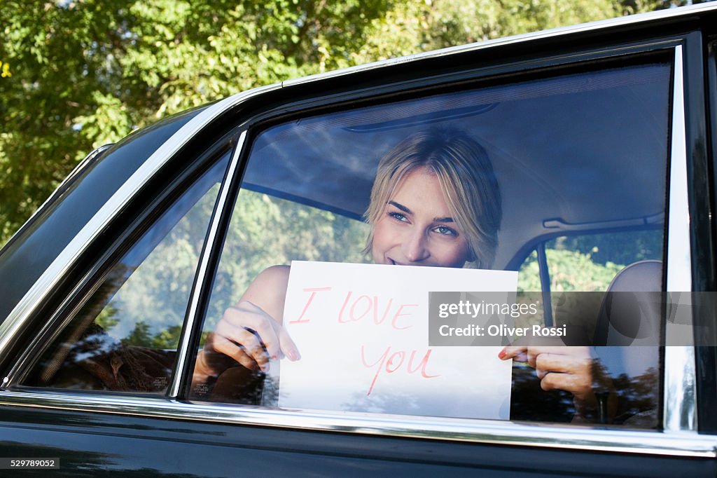 Young woman holding a sign saying "I Love You" up to a car window