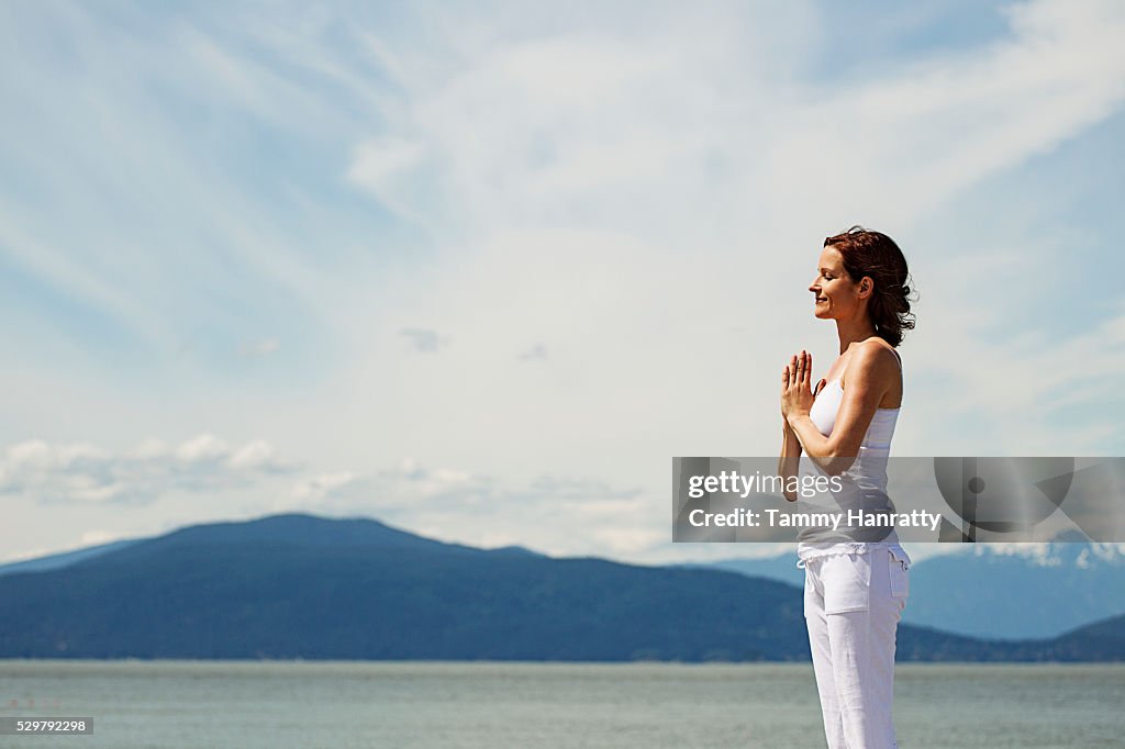 Mid-adult woman meditating while practicing yoga at sea