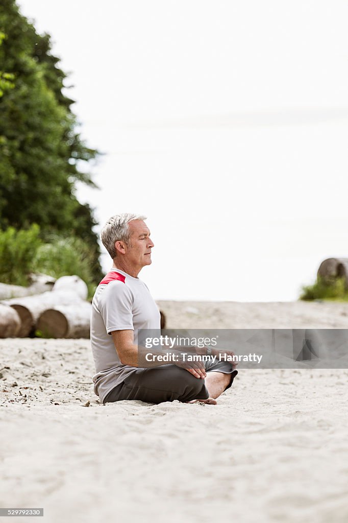 Senior man sitting on sand and practicing yoga