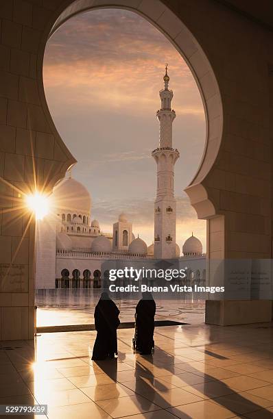 two arab women entering a mosque at sunset - arab woman walking stock-fotos und bilder