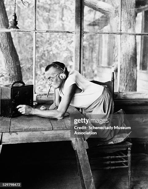 Dr. Charles P. Steinmetz kneels on a chair to adjust a radio tuner. Steinmetz, an engineer at General Electric, created calculations for predicting...