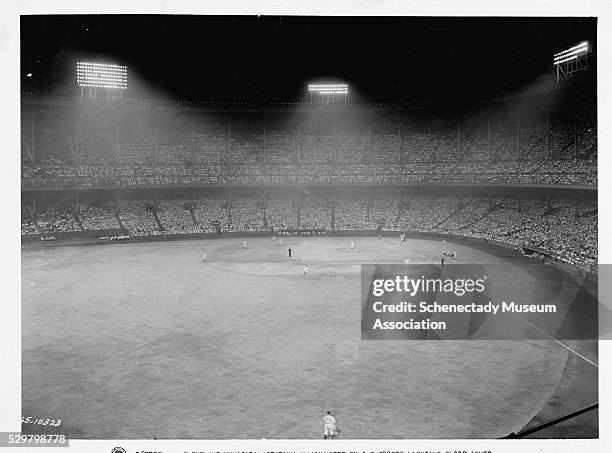 The Cleveland Municipal Stadium is illuminated with General Electric sport floodlights during a major league baseball game. This game was attended by...