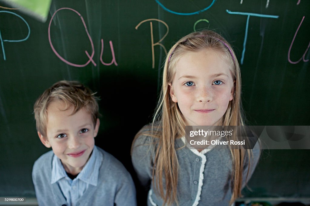 Schoolboy (6-7) and girl (8-9) posing in front of blackboard
