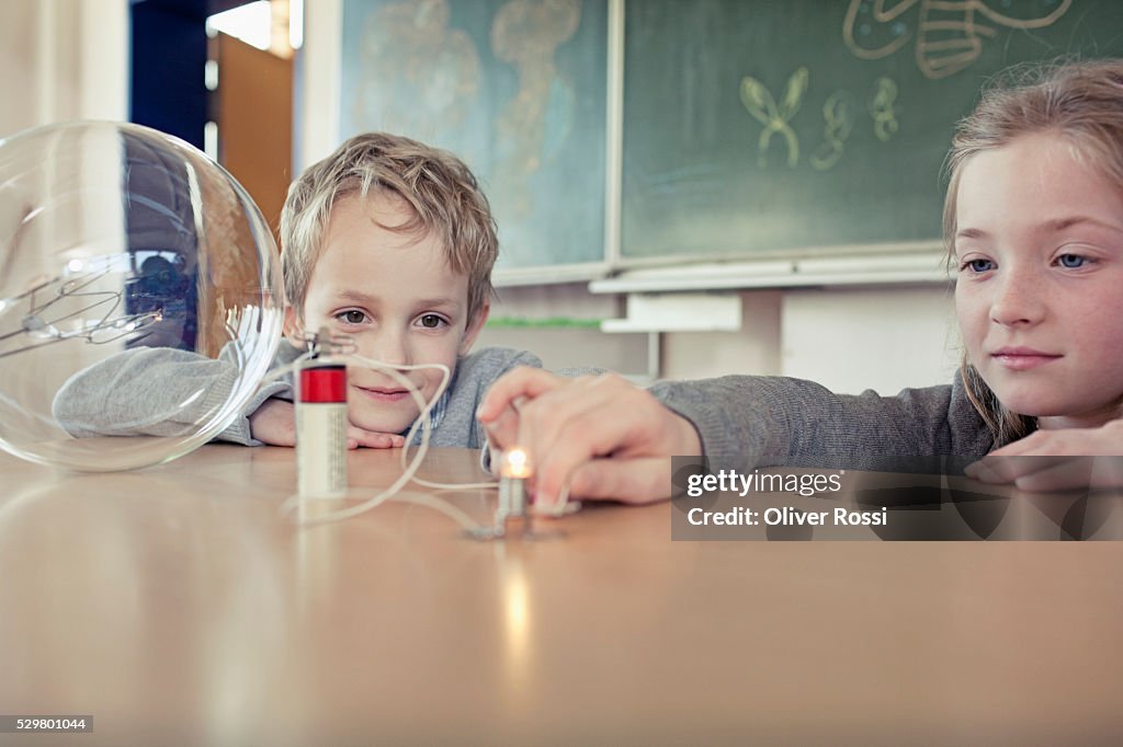 Schoolgirl (6-7) and boy (6-7) experimenting with electricity in science class