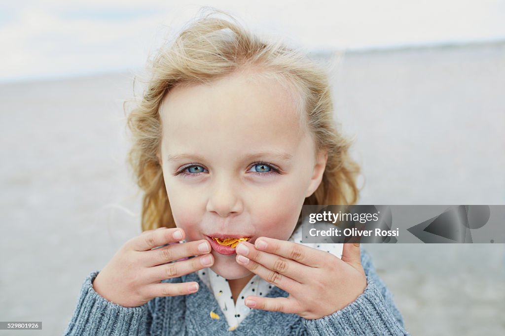 Blond girl eating chips on the beach