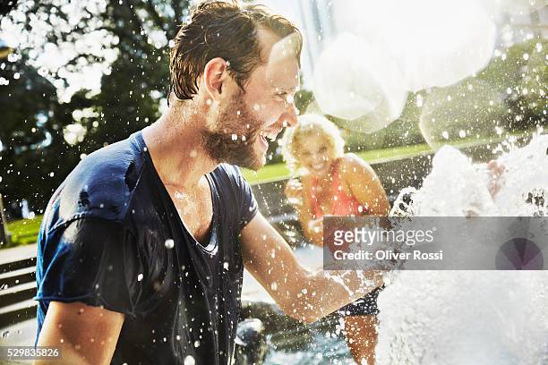 couple splashing in water of fountain - man splashed with colour fotografías e imágenes de stock