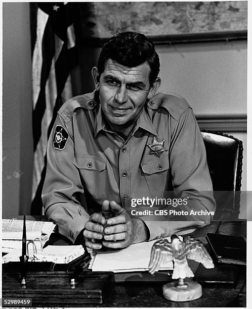 American actor Andy Griffith sits in uniform behind a desk on the set of his television series 'The Andy Griffith Show,' 1967.